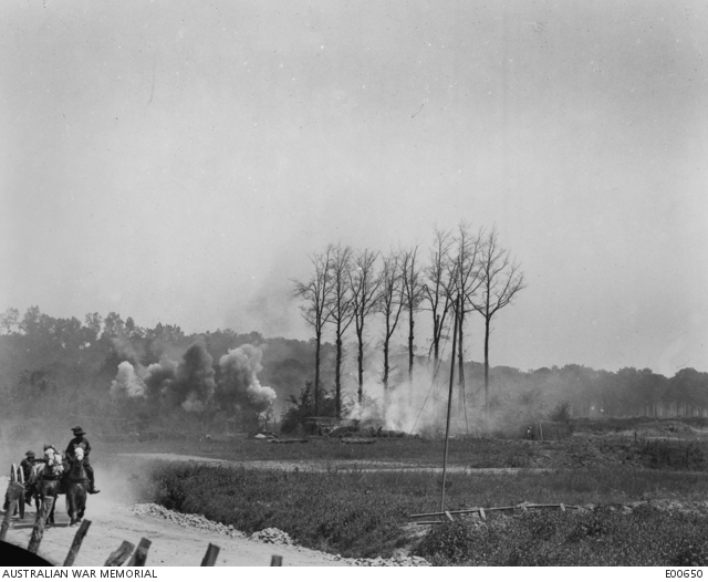 An Australian transport wagon, galloping along the road near Red Lodge, behind Hill 63, in Belgium, whilst the Germans were shelling the batteries of the Australian and New Zealand Artillery concentrated there for the battle of Messines, which opened on 7 June 1917. Note that enemy shelling has set fire the camouflage over the guns. The gunners may be observed endeavouring to put out the fire although the position was still being shelled.